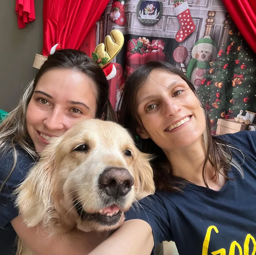 Duas cuidadoras da Good Times abraçadas com um golden retriever