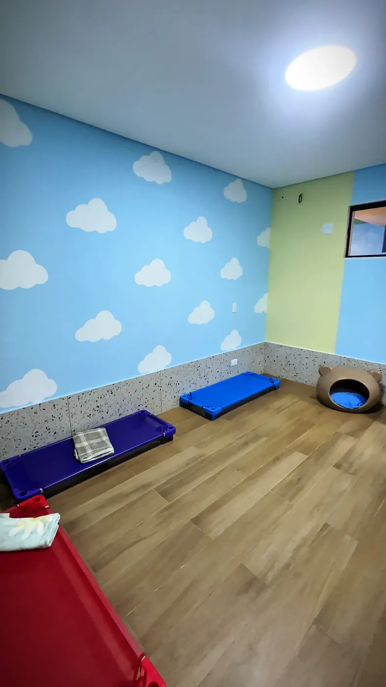 Quarto do hotel com parede azul-céu pintada de nuvens, piso de madeira, caminhas coloridas e uma toca